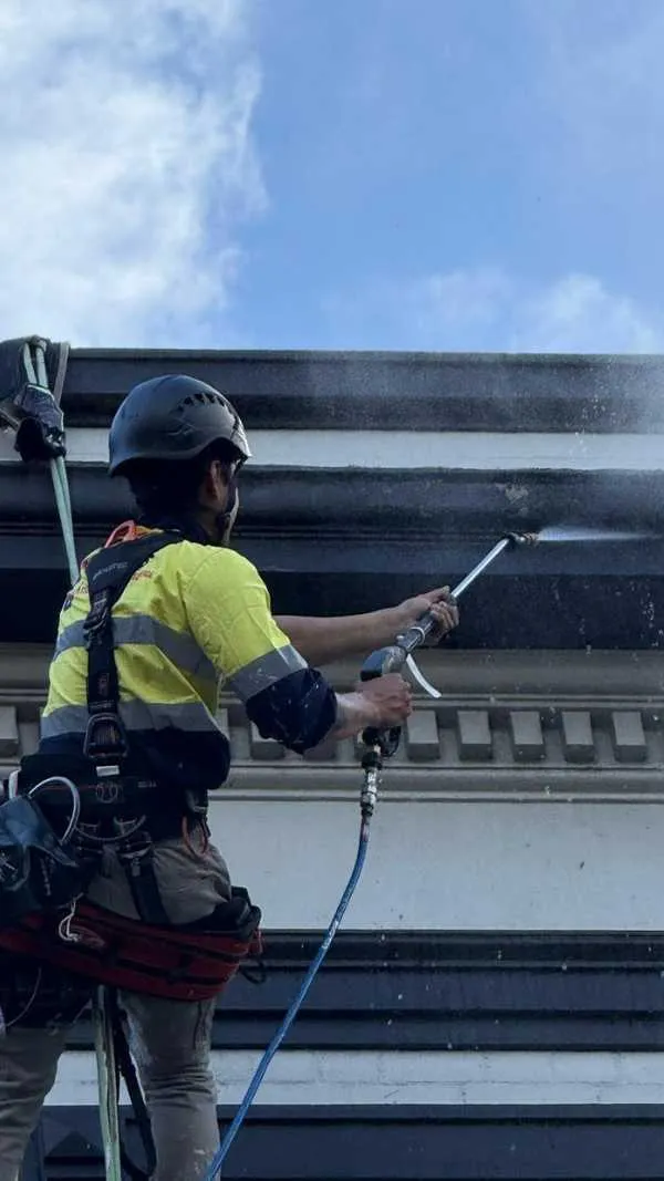 Rope access technician pressure washing a building facade
