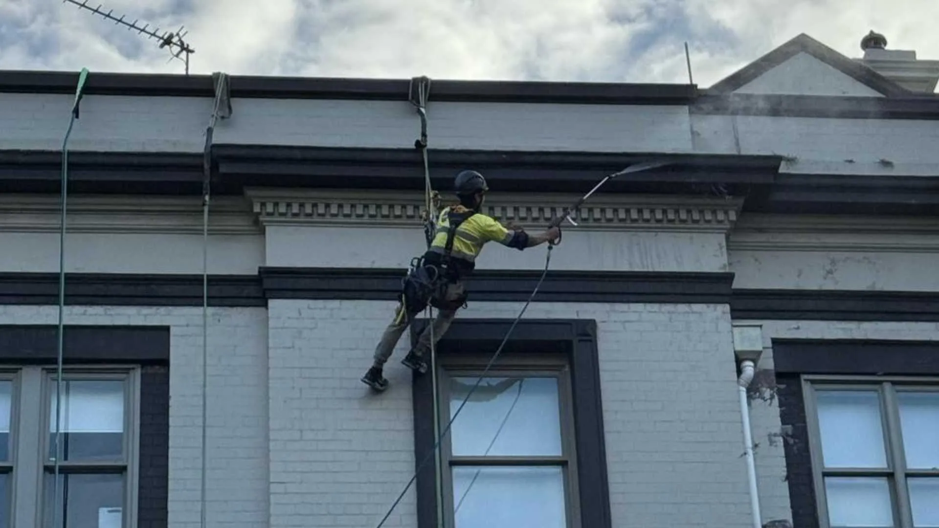 Rope access technician pressure cleaning the parapet of a heritage building